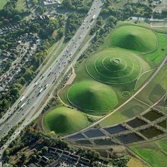 an aerial view of some green mounds in the middle of a road with cars driving on it