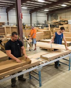 two men working in a factory with wooden planks on the floor and one man holding a piece of wood