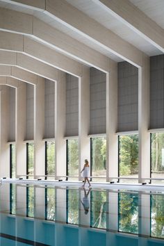 a woman is walking in front of a swimming pool with large windows on both sides