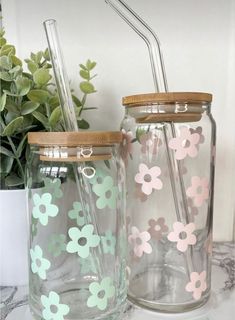 two mason jars with flowers painted on them, one has a straw and the other has a lid