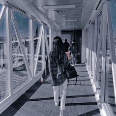 a woman walking down a long hallway next to tall glass windows on top of a building