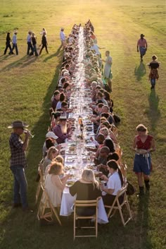 a long table with many people sitting at it in the middle of a grassy field