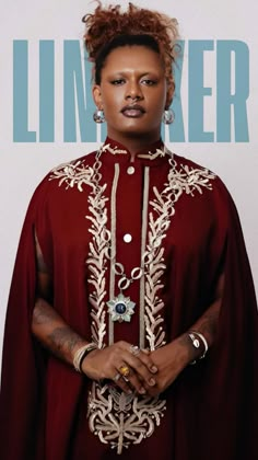 a woman wearing a red cape and jewelry standing in front of a white wall with the word limiter on it