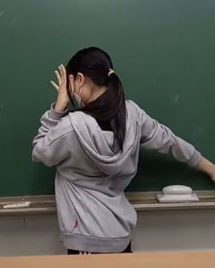 a woman standing in front of a blackboard holding her hands to her head and covering her eyes