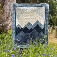 a blue and white quilt is hanging on a tree in a field with wildflowers