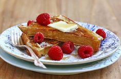 french toast with butter and raspberries on a blue and white plate next to a fork