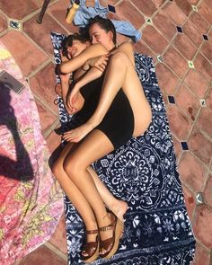 two women in swimsuits are laying on a towel and one is hugging the other