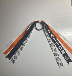 Ponytail ribbons are a cute way to show team spirit! These are great for individuals, teams and coaches! There are 2 ribbon lengths to choose from, 7 inch and 9 inch (each ribbon side is 7 or 9 inch making for a total of 14 or 18 inches). The ribbon sizes vary in size from 3/8" - 7/8". Each ponytail has 4 ribbons on each side for a total of 8 per ponytail. I use quality grosgrain ribbon. The ribbons are held together with a zip tie and a ribbon is used to cover the zip tie so it's not seen but really is built to last! Each ribbon ordered has the option to be a ribbon in team colors, ribbon with a name and sports ball image or ribbon with name, sports ball image and number. There are many different colors of ribbon and personalization colors to choose from.  Many different sports options to Volleyball Hair Ribbons, Hair Ribbons Diy, Ribbon With Name, Cheer Ponytail, Volleyball Ribbon, Basketball Hair, Ribbon Hair Tie, Sports Hair, Volleyball Hair