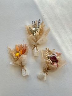 three bouquets of dried flowers tied to burlap paper on a white surface