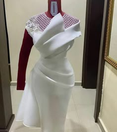 a white dress on display in a room with a red and white coat hanging from it's back