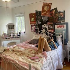 a woman laying on top of a bed next to a wall covered in pictures and posters