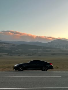 a black car is parked on the side of the road in front of some mountains