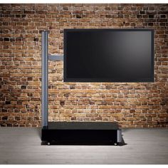 a flat screen tv sitting on top of a metal stand in front of a brick wall