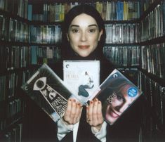 a woman holding two cd's in front of a bookshelf