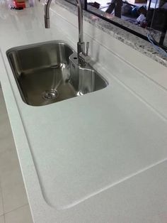 a stainless steel sink in a kitchen with white counter tops and tile flooring on the walls