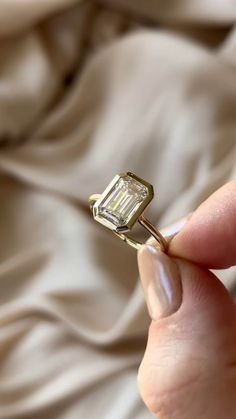 a person holding a ring with a diamond in it's middle, on top of a bed