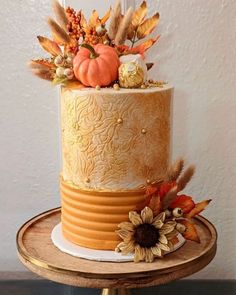 a three tiered cake decorated with fall leaves and pumpkins on a wooden stand