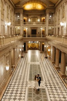 a bride and groom standing in the middle of a large hall with black and white checkered floor