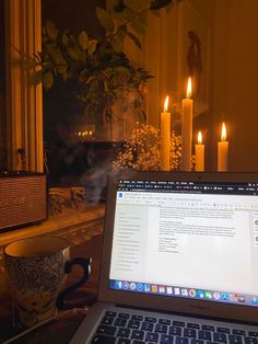 an open laptop computer sitting on top of a table next to a candle lit room