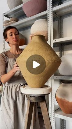 a woman standing next to a vase on top of a wooden stool in front of shelves