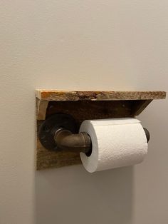 a toilet paper dispenser mounted on a wall with a wooden shelf above it