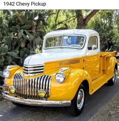 an old yellow truck is parked on the side of the road in front of some trees