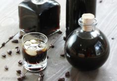 two bottles and a glass filled with liquid sitting on a table next to coffee beans