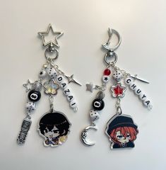 two keychains with charms attached to them on a white surface, one has an anime character and the other has a name