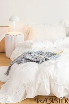 an unmade bed with white sheets and pillows on the floor next to a lamp