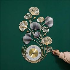 a person is pointing to a clock on the wall with flowers in front of it