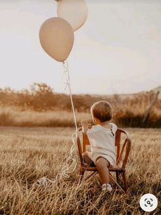 a little boy sitting in a chair with two balloons