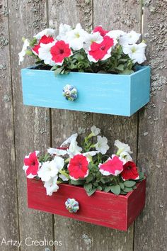 two wooden boxes with flowers in them hanging on the side of a fence, one blue and one red