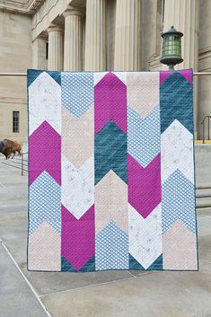 a very pretty quilt on the ground by some steps with a building in the background