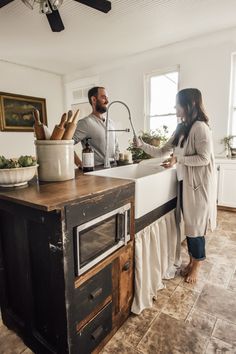 a man and woman standing in front of a kitchen sink next to a counter top