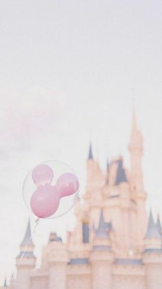 a person is flying a pink mickey mouse balloon in front of the disney world castle