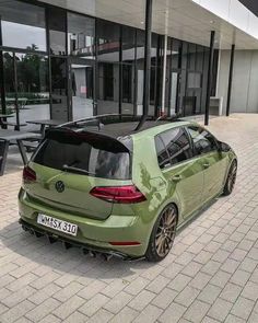 a green car is parked in front of a building with glass doors and large windows