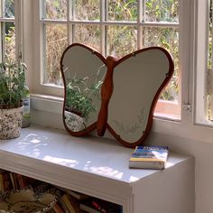 a butterfly shaped mirror sitting on top of a window sill next to a potted plant