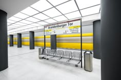 an empty train station with yellow and white signs on the wall next to metal barriers