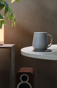 a coffee cup sitting on top of a white table next to a speaker and a potted plant