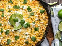 a skillet filled with corn and topped with cilantro, sour cream and lime