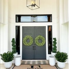 the front door is decorated with wreaths and two potted plants on either side