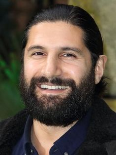 a man with a beard smiles at the camera while wearing a blue shirt and black jacket