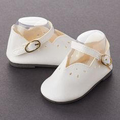 a pair of white baby shoes with gold buckles on the front and back straps