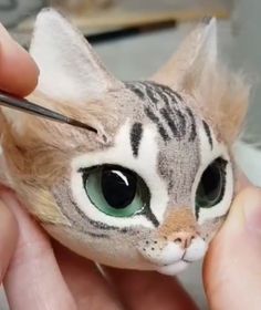 someone is painting a cat's face with green eyes