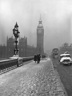 two people walking down a snowy street in front of big ben and the houses of parliament