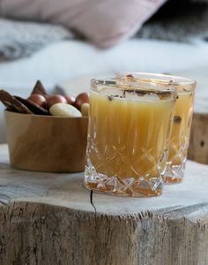 a glass filled with liquid sitting on top of a wooden table next to a bowl of nuts