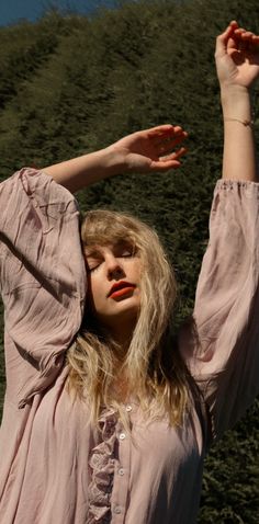 a woman in a pink dress is holding her hands up to the side with one hand