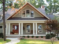 a gray house with white pillars and two large windows on the front porch, surrounded by trees