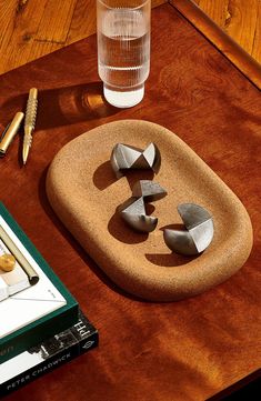 three pieces of metal sitting on top of a wooden table next to a glass and pencils