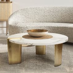 a white marble coffee table with gold legs and a bowl on top in front of a couch